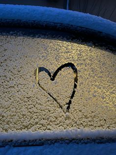 a heart drawn on the windshield of a car covered in ice and snow at night