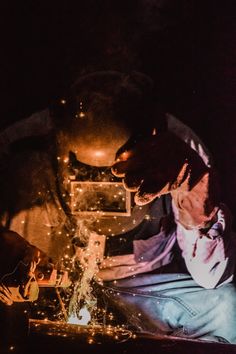 a man working on something in the dark with his hands and face lit by lights