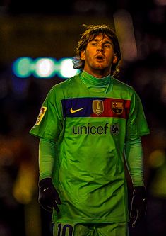 the soccer player is wearing green and blue uniform with his hand on his hip as he stands in front of an audience