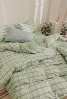 an unmade bed with green and white plaid sheets