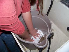 a woman is washing her hands in a bucket filled with white soap and brown stuff