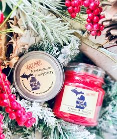 two jars of candles sitting on top of a table next to berries and pine cones