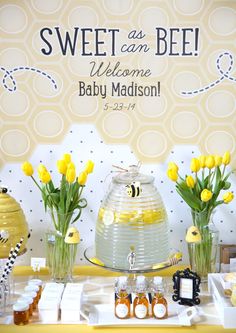 a table topped with vases filled with yellow flowers and honeycombs next to a sign that says, sweet as can bee welcome baby madison