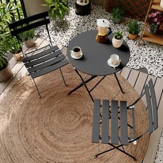 an outdoor patio with two chairs and a round rug on the floor, surrounded by potted plants