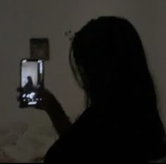 a woman is taking a photo with her cell phone in the dark while sitting on a bed