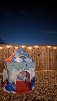 a tent in the sand with string lights on it and a wooden fence behind it