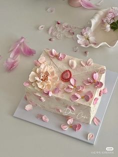 a white cake with pink flowers and petals on the top is sitting on a plate