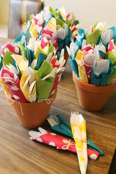 small pots filled with colorful paper flowers on top of a wooden table next to utensils