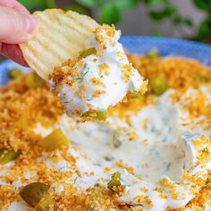 a hand holding a cracker over a bowl of dip