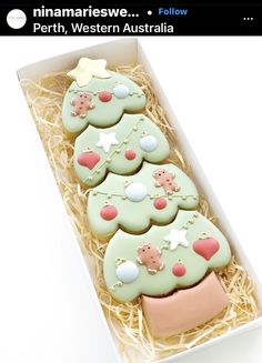 three decorated cookies in a box with straw on the bottom and one is pink, white and green