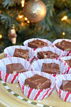 several pieces of chocolate in paper wrappers on a platter next to a christmas tree