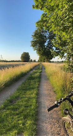 a bike parked on the side of a dirt road next to a lush green field