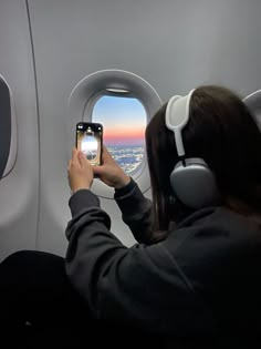 a woman is taking a photo with her cell phone while sitting in an airplane window