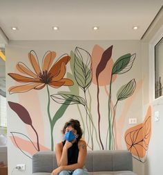 a woman sitting on top of a couch next to a wall with flowers painted on it