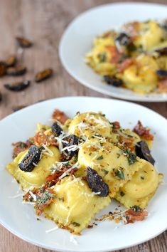 two white plates topped with ravioli covered in cheese and olives on a wooden table