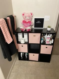 a pink teddy bear sitting on top of a black shelf next to some towels and toilet paper