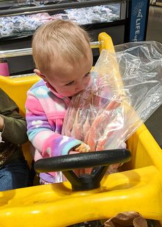 a baby sitting in a yellow toy car with plastic bags on it's back