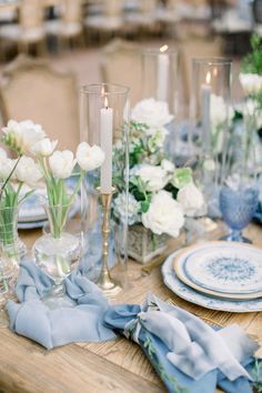 the table is set with blue and white plates, napkins, flowers and candles