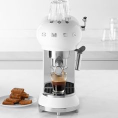 an espresso machine sitting on top of a counter next to some cookies and coffee