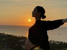 a woman standing in front of the ocean with her arms spread out to the side