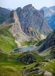 the mountains are covered in green grass and there is a small lake at the bottom