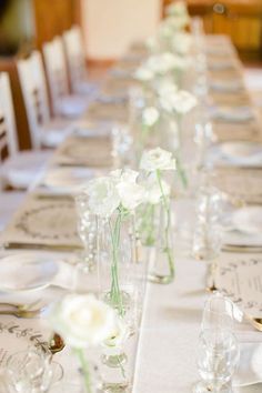 a long table with white flowers in vases and place settings on the top row