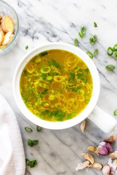 a white bowl filled with soup next to some garlic and green onions on a marble surface