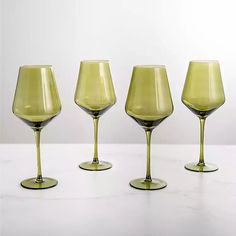 four yellow wine glasses lined up on a white counter top with one empty glass in the middle