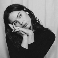 a black and white photo of a woman with her hand on her chin looking at the camera