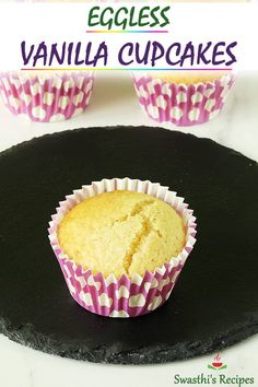 two vanilla cupcakes sitting on top of a black plate with pink and white paper wrappers