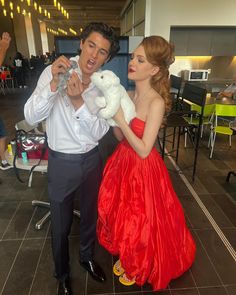 a man holding a stuffed animal next to a woman in a red dress