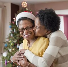 two women hugging each other in front of a christmas tree