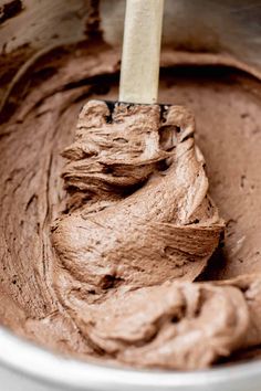 a wooden spoon in a bowl filled with chocolate frosted cake batter on top of a table