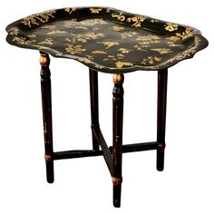 a black and gold tray with flowers on the bottom is sitting on a stand that has two legs