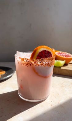 a pink drink with orange slices and cinnamon sprinkles on the rim next to a cutting board