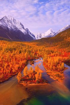 an aerial view of a river surrounded by trees with snow capped mountains in the background