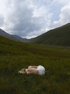 a person laying on the ground in a grassy field with mountains in the backgroud