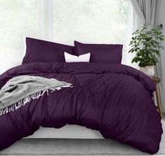 a bed with purple comforter and pillows in front of a white window sill