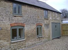 an old stone house with three windows and graveled driveway area in front of it