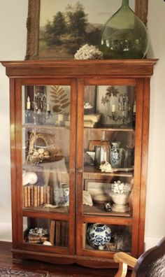 an antique china cabinet with glass doors and shelves filled with vases, books, and other decorative items