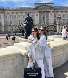 two women standing next to each other in front of a large building with statues on it