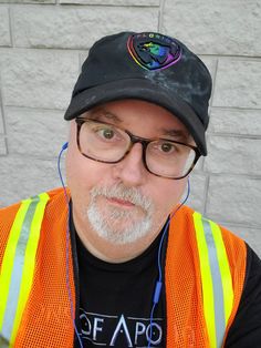 a man in an orange vest and black hat with ear buds on his ears wearing headphones