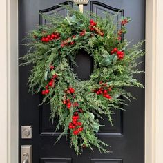 a christmas wreath hanging on the front door with holly and red berries, greenery