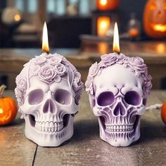 two skulls with candles in the shape of heads on a wooden table next to pumpkins