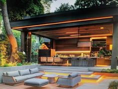 an outdoor living area with couches, tables and lights on the outside wall is lit up at night