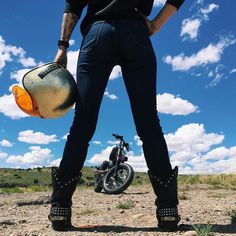 a person standing next to a motorcycle on a dirt field with clouds in the background