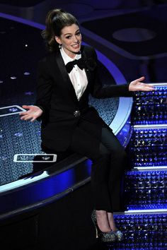 a woman in a tuxedo sitting on top of a table with her hands out