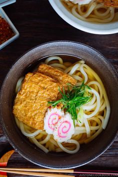 two bowls filled with noodles and meat on top of a wooden table next to chopsticks