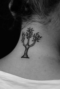 a woman's neck with a small tree tattoo on the back of her neck