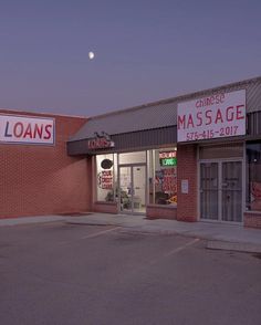 an empty parking lot in front of a chinese massage shop at night with the moon shining